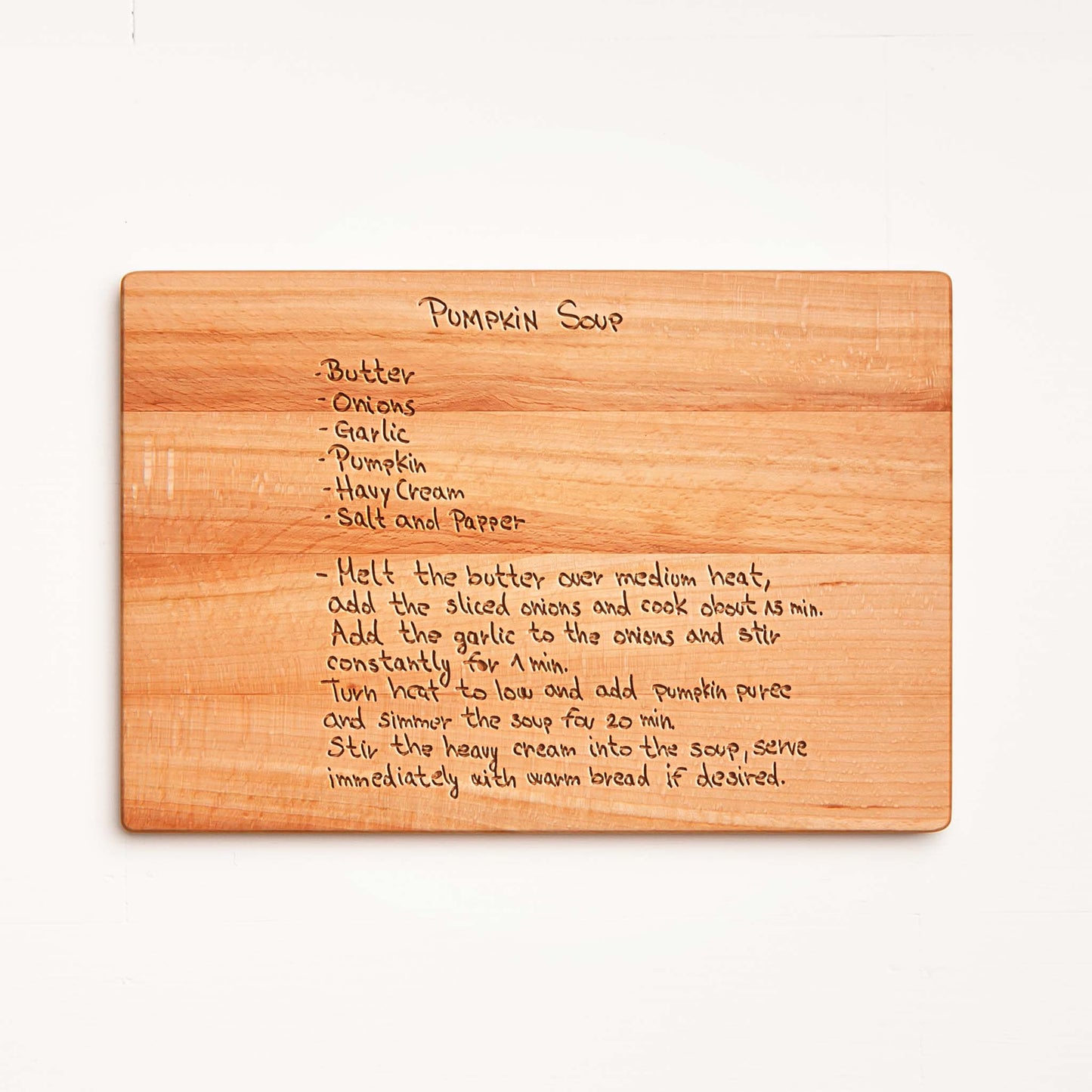 Wooden cutting board with engraved pumpkin soup recipe on a white background