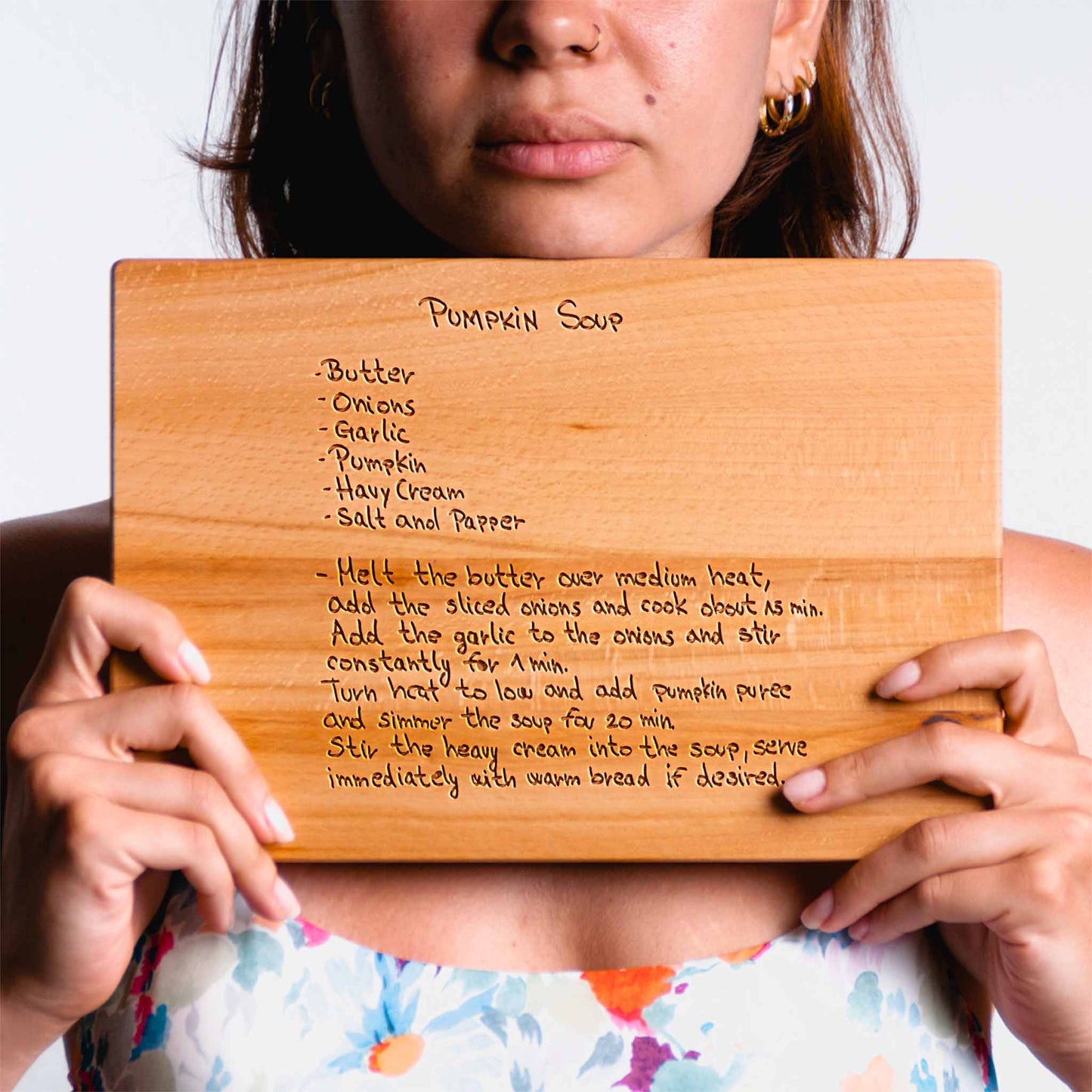 Person holding a wooden cutting board with pumpkin soup recipe