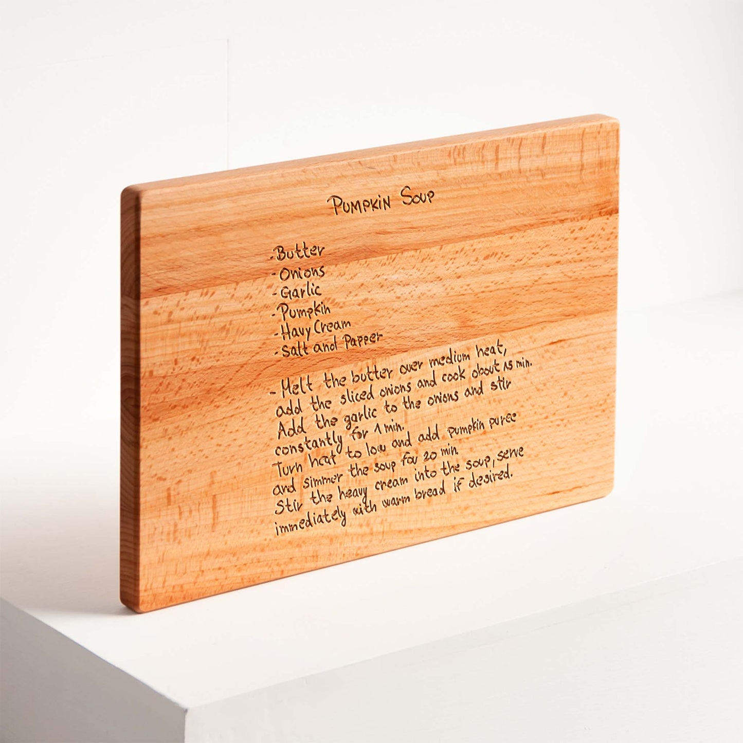 Wooden cutting board with engraved pumpkin soup recipe on a white background