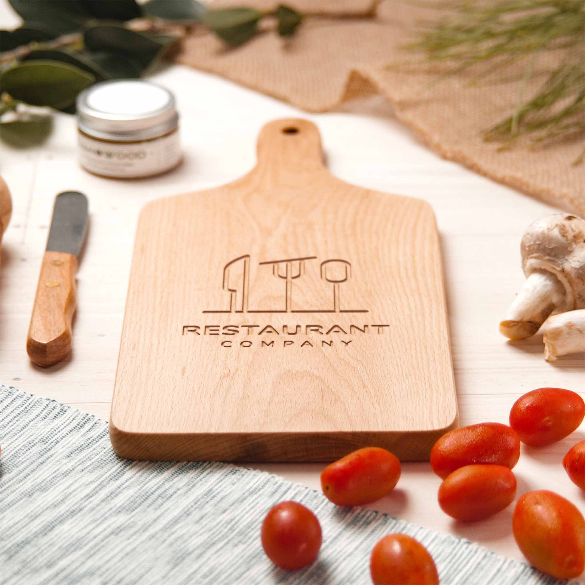 Wooden cutting board with engraved logo on a table with tomatoes and other items