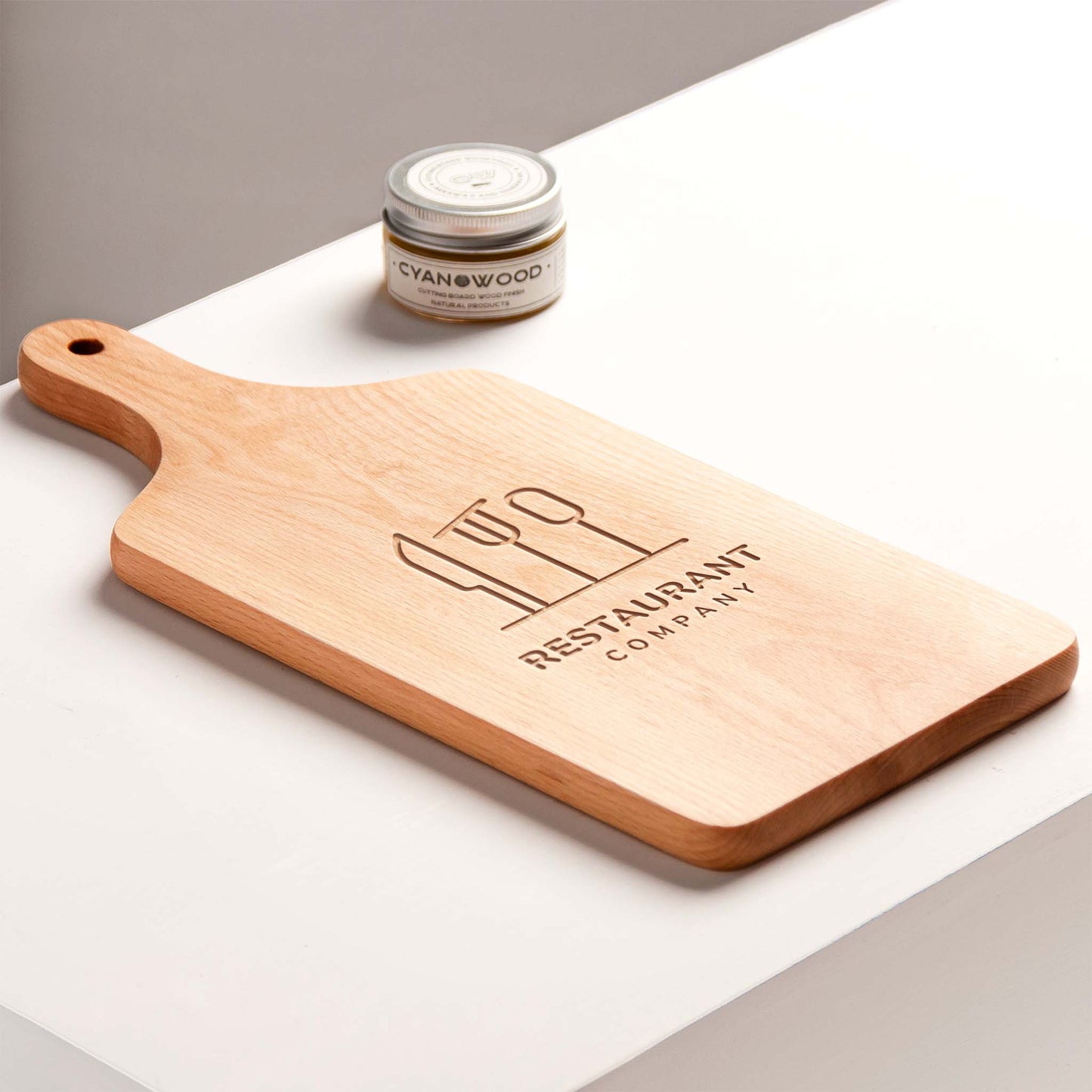 Wooden cutting board with engraved text on a white surface, featuring a jar of wood care product.