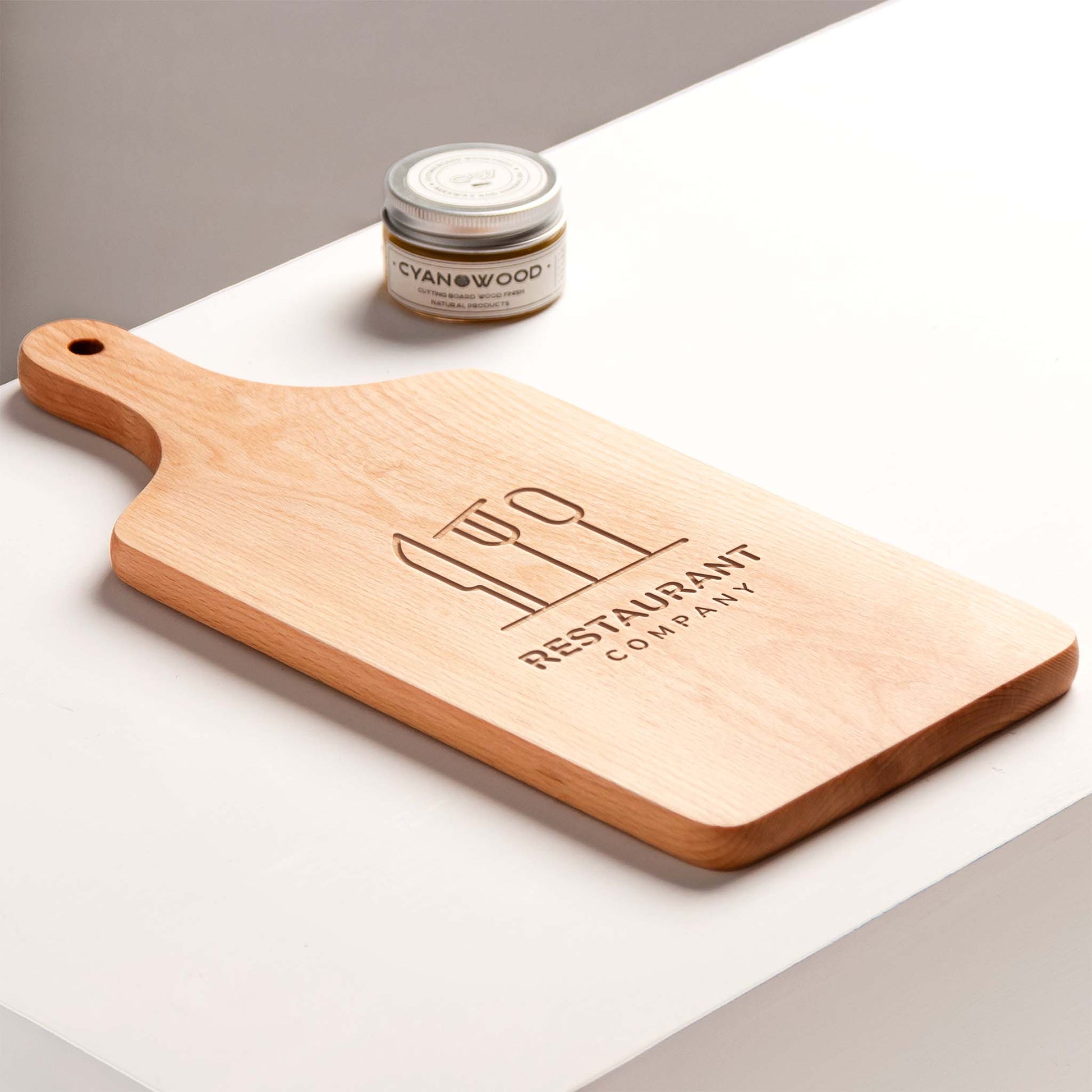 Wooden cutting board with engraved text on a white surface, featuring a jar of wood care product.