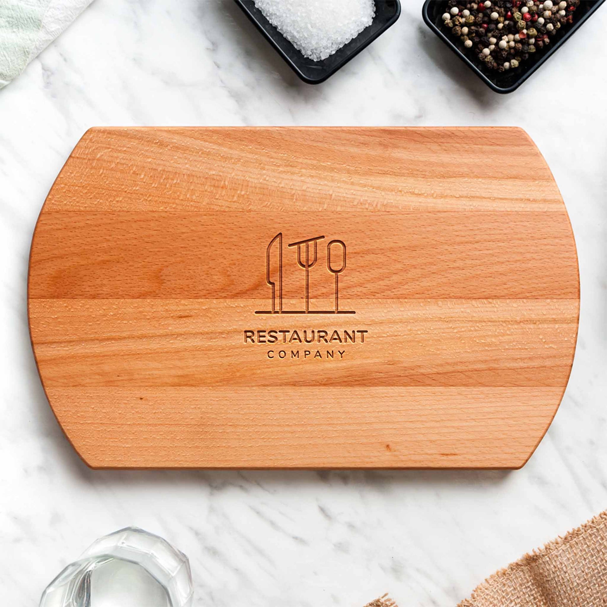 Wooden cutting board with engraved logo and text on a marble surface