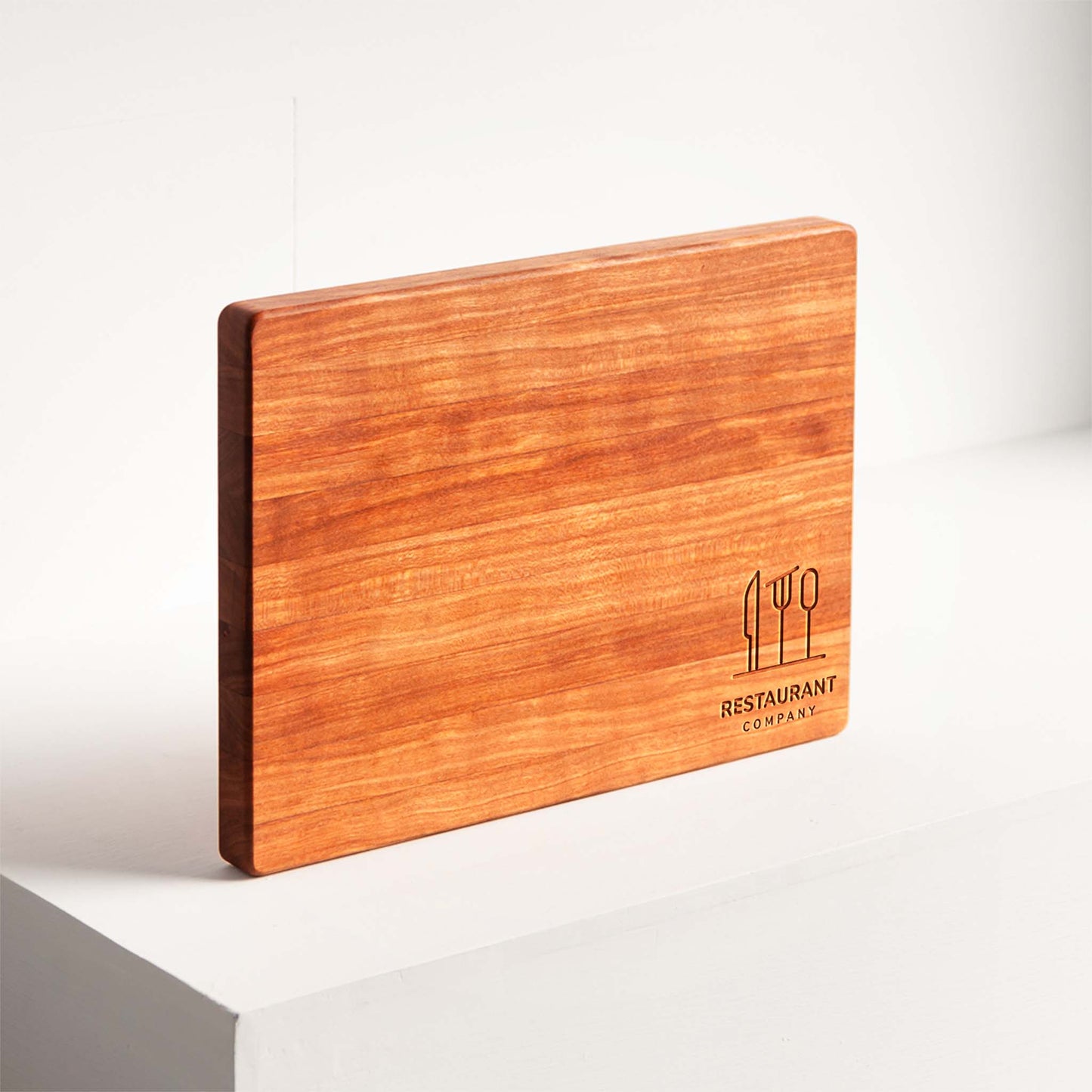 Wooden cutting board with engraved logo on a white surface