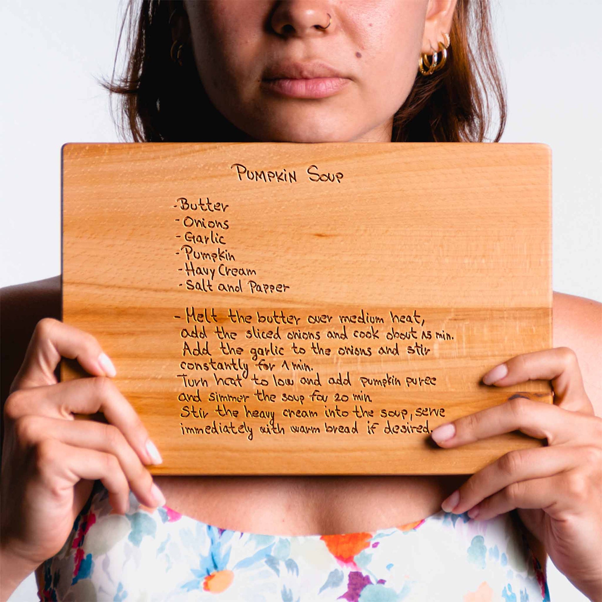 Person holding a wooden cutting board with pumpkin soup recipe