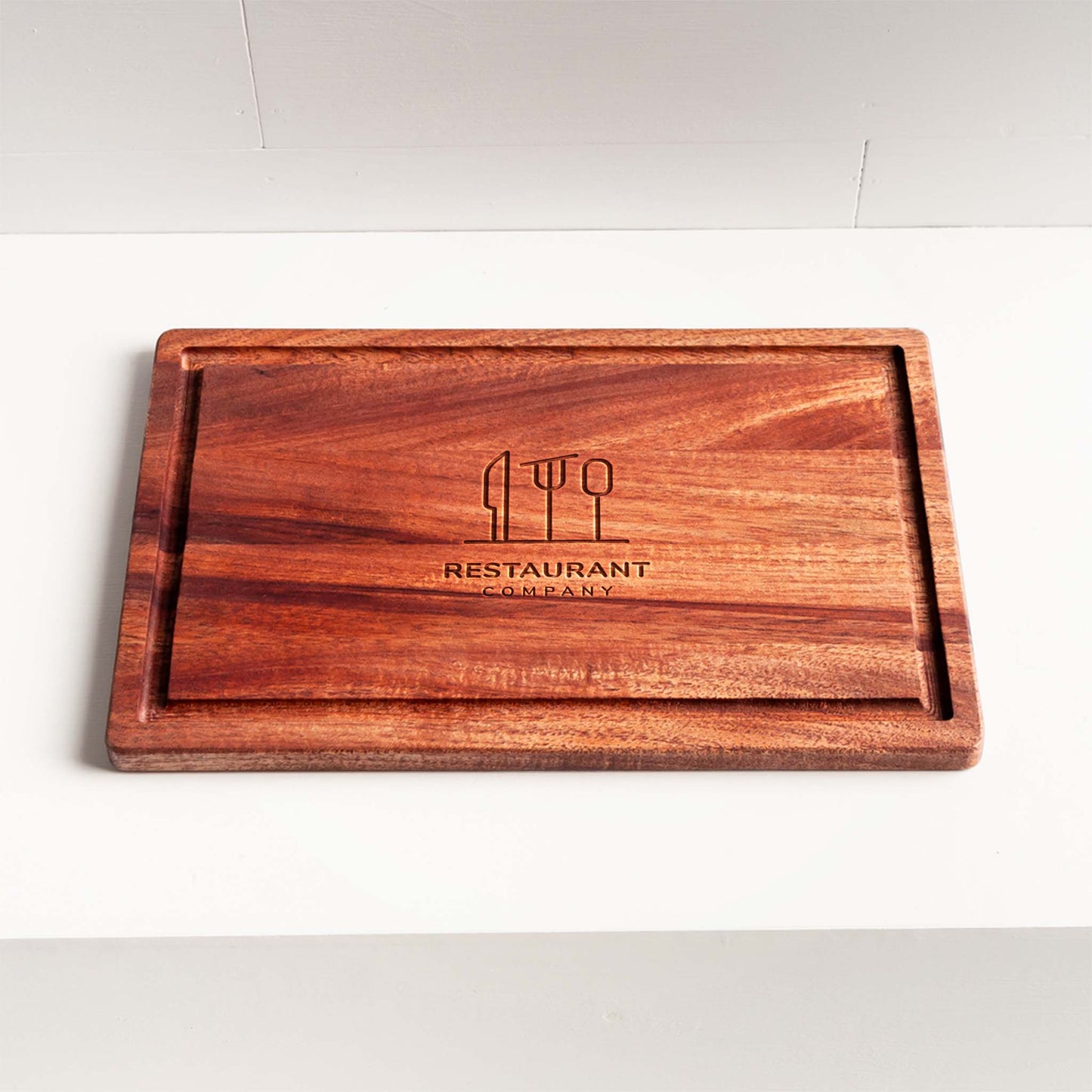 Rectangular mahogany cutting board with juice groove and engraved restaurant logo.