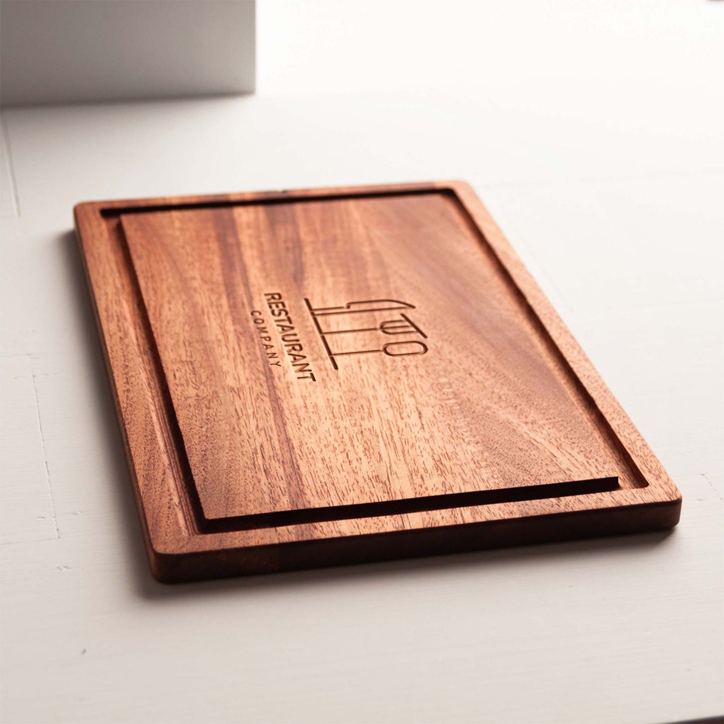 Rectangular mahogany cutting board with juice groove and engraved restaurant logo.