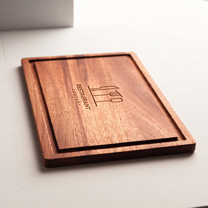 Rectangular mahogany cutting board with juice groove and engraved restaurant logo.